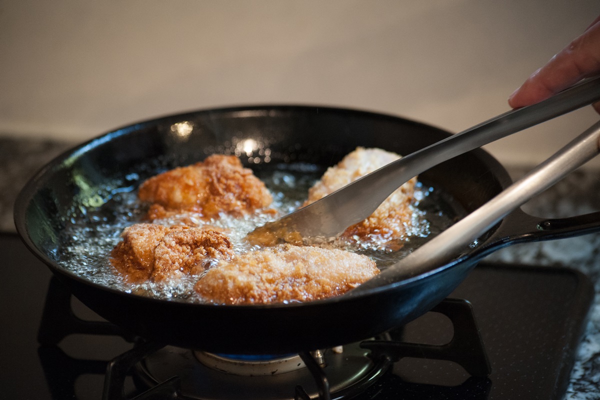 Foto colorida. Imagem mostra uma frigideira no fogão com gordura quente fritando frangos - Metrópoles