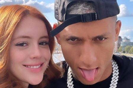 Amanda Araújo e Richarlison em foto colorida. Ela é uma mulher jovem, branca, do cabelo ruivo. Ele está de boné preto, língua para fora e camisa preta, com cordão prata - Metrópoles