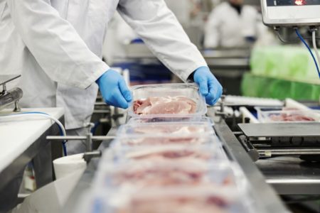 Funcionário de frigorífico, com avental branco e luvas azuis, manipula carne embalada - Metrópoles