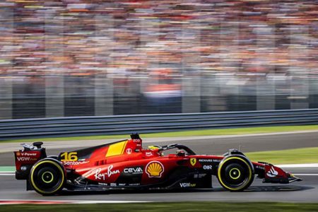 Imagem colorida de Ferrari vermelha em alta velocidade enquanto torcida embaçada torce no fundo da foto - Metrópoles