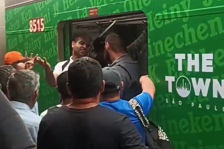 Em foto colorida homem de caliseta branca argumenta com segurança da ViaMobilidade na entrada de um vagão, no qual há a logo do festival The Town - Metrópoles