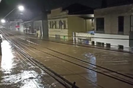 Imagem colorida de uma rua alagada, com água que chega a altura das casas - Metrópoles