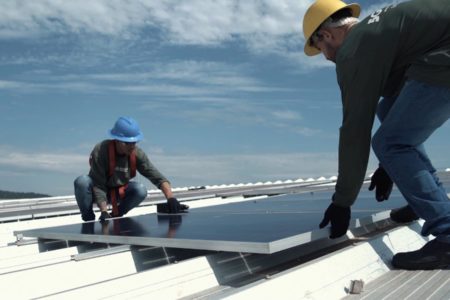 Fotografia colorida de dois homens instalando um painel de energia solar