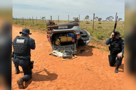 Imagem colorida de policiais armados e carro de traficante capotado - Metrópoles