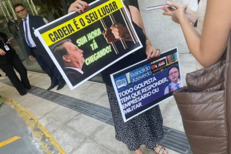 Imagem colorida mostra uma mulher segurando dois cartazes de protesto contra o ex-presidente Jair Bolsonaro em frente a um hospital - Metrópoles