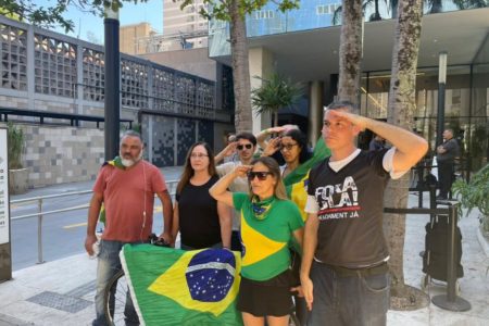 Imagem colorida mostra apoiadores do ex-presidente Jair Bolsonaro na frente do hospital onde ele está internado. O grupo segura uma bandeira do Brasil e um deles bate continência - Metrópoles