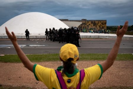 imagem de mulher de braços abertos olhando para policiais e congresso nacional em 8 de janeiro