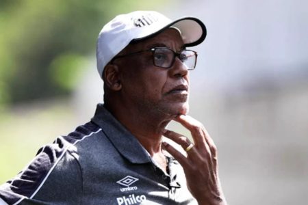 foto colorida mostra Serginho Chulapa usando boné branco do Santos, camiseta escura, óculos e mão no queixo - Metrópoles
