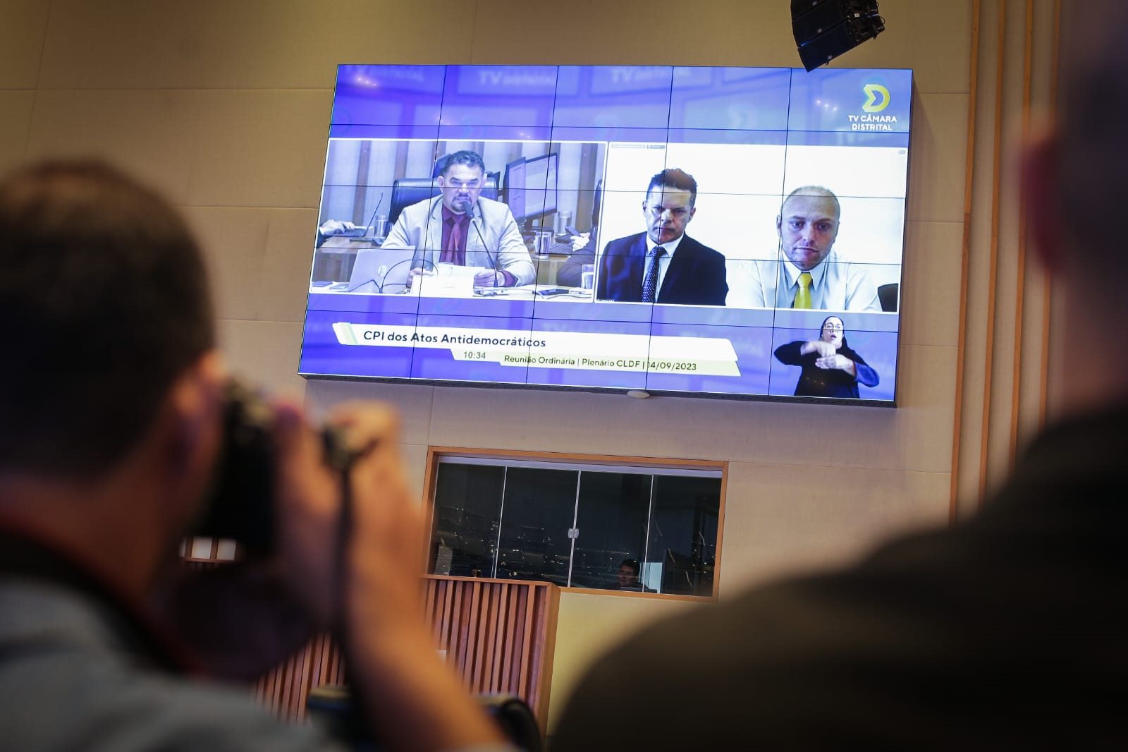 Telão com homens conversando é observado por fotógrafo