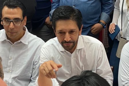 Foto colorida de homem branco com cabelo preto e camisa branca, sentado, olhando para o lado - Metrópoles