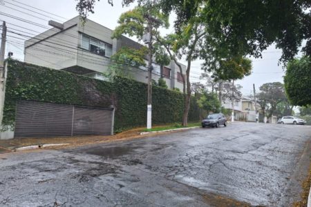 Imagem colorida mostra a rua em que mora o ministro Fernando Haddad, com árvore na frente da casa e asfalto molhado por conta da garoa - Metrópoles