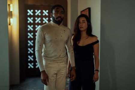 Donald Glover e Maya Erskine em Sr. & Sra. Smith. Um homem preto com roupa clara ao lado de uma mulher branca com vestido preto - Metrópoles