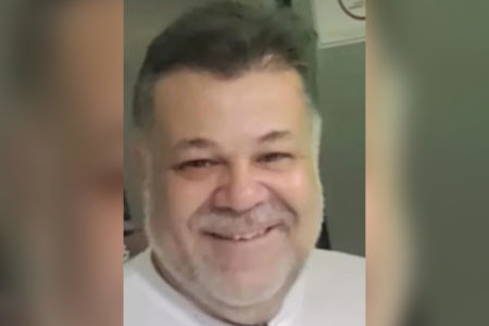 Foto colorida mostra homem de cabelo preto e barba grizalha sorrindo enquanto olha para a câmera