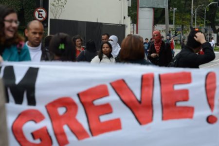 imagem colorida mostra cartaz de greve e pessoas ao fundo reajuste servidores - metrópoles