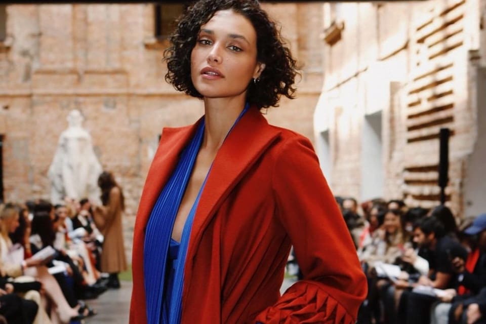 Débora Nascimento posa com uma blusa azul e um blazer vermelho - Metrópoles