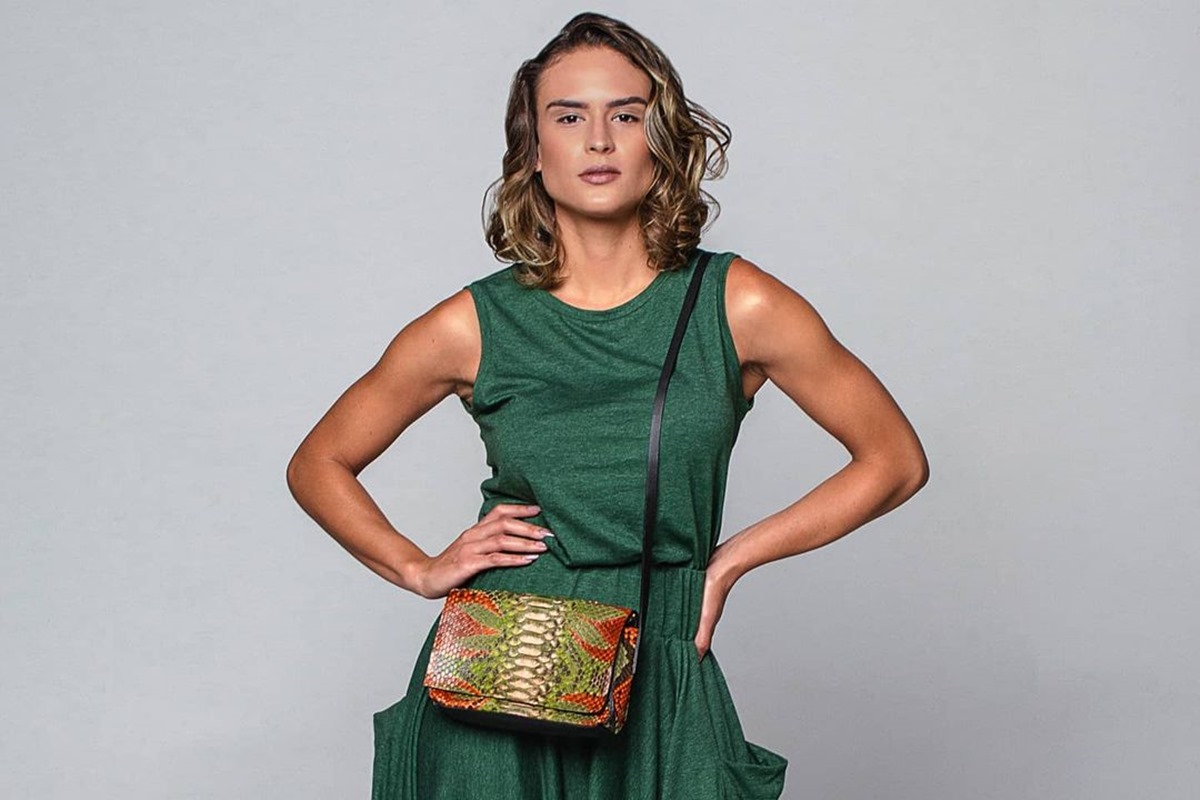 Mulher com vestido verde posando em frente a fundo cinza. Ela está segurando a cintura com as duas mãos - Metrópoles