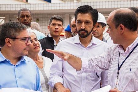 Imagem colorida mostra Ricardo Nunes, homem branco de cabelo e barba pretos, vestindo camisa branca, cercado de outros homens gesticulando com as mãos, em uma visita a obra pública - Metrópoles