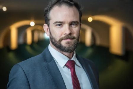 Foto posada de Dario Durigan, secretário reforma administrativa -executivo do Ministério da Fazenda. Ele veste uma camisa branca, gravata vermelha e terno azul claro, e tem barba - Metrópoles