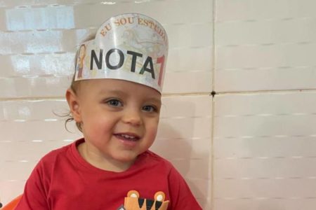 Criança sorrindo com um chapéu de papel escrito "u sou estudante nota 1"