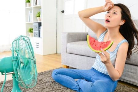 Mulher com calor segurando uma melancia e ventilador