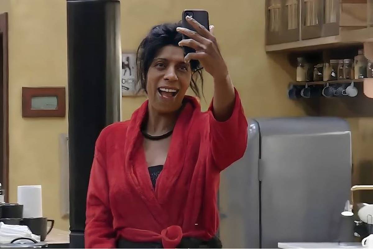 foto colorida de mulher negra de roupão vermelho segurando celular - metrópoles