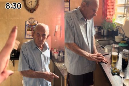 Foto colorida de um idoso comendo azeitona e bebendo cerveja na cozinha - Metrópoles