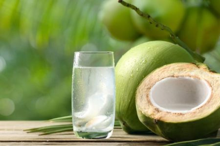 Agua de coco em um copo de vidro e com um coco verde ao lado