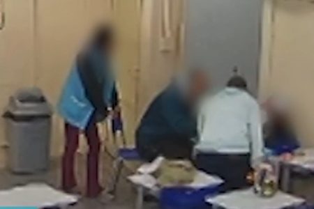 foto colorida mostra dois professores de pé cercando aluno sentado em sala de aula; uma terceira professora observa a distância - Metrópoles