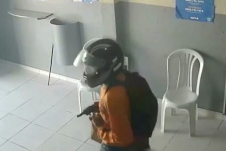 Um homem de capacete de motociclista está segurando uma arma de fogo