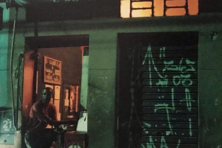 Imagem mostra homem em pé na frente do bar, à noite