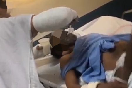 Em foto colorida homem com braço engessado dá colida na boda de senhor amarrado em cama de hospital - Metrópoles