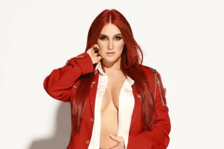 Foto colorida de Dulce María com o cabelo vermelho, a jaqueta aberta e a mão no rosto - Metrópoles