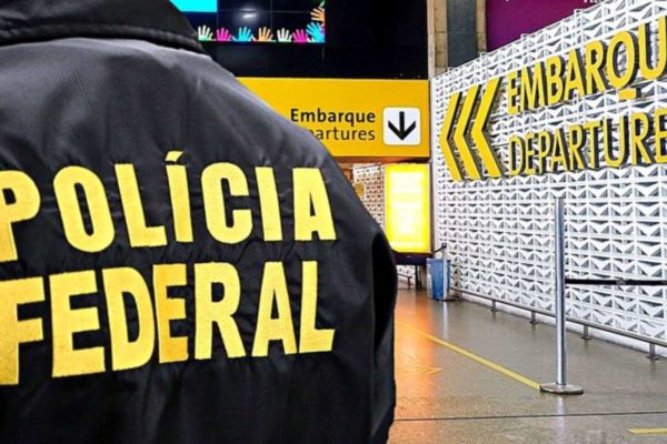 Imagem colorida de agente da polícia federal de costas no aeroporto internacional de são paulo em guarulhos - Metrópoles