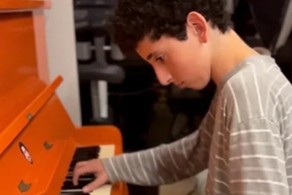 Foto colorida de Stefano Mion. É uma criança branca, de cabelo preto e moletom cinza tocando piano - Metrópoles