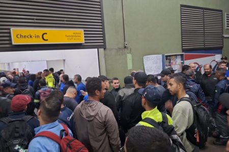 Em foto colorida pessoas aglomerada em frente de placa amarela - Metrópoles