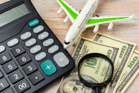 uma calculadora ao lado de um avião miniatura com dólares e uma lupa em cima da mesa