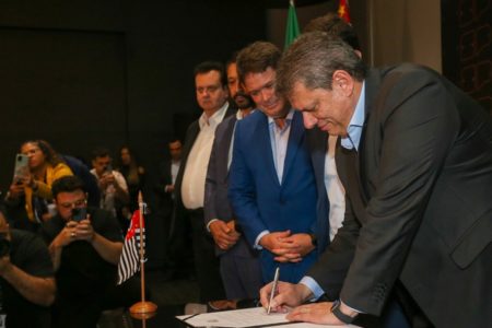 Fotografia colorida mostra Arthur Lima observando Tarcísio de Freitas assinar um documento - Metrópoles