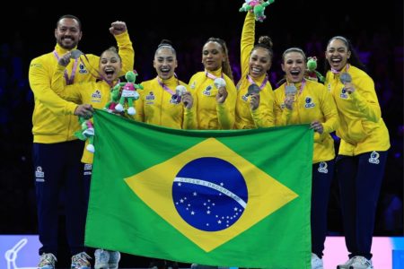 Imagem mostra time feminino de ginástica artística do Brasil posando com bandeira do Brasil- Metrópoles