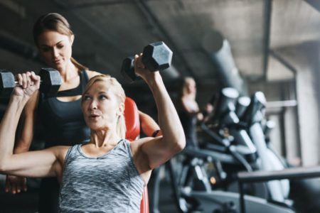 Mulher treinando com pesos na academia juntamente com uma personal treiner