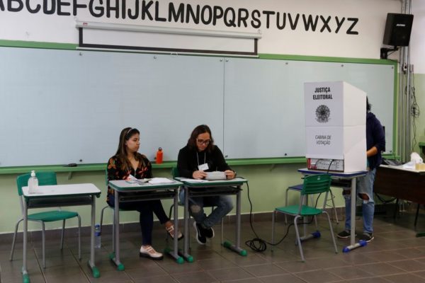 foto colorida de eleição do Conselho Tutelar em SP; detalhe com imagem da urna e mesários - Metrópoles