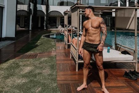 Foto colorida de homem com sunga preta em frente à piscina - Metrópoles