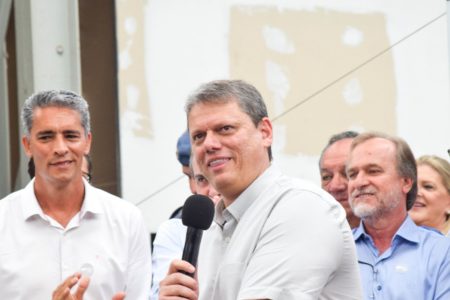 Imagem colorida mostra Tarcísio de Freitas, homem branco e grisalho, de camisa branca, falando ao microfone, cercado de aliados políticos - Metrópoles