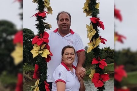 Imagem colorida de casal vestidos de branco em fundo verdes e com flores ao redor - Metrópoles