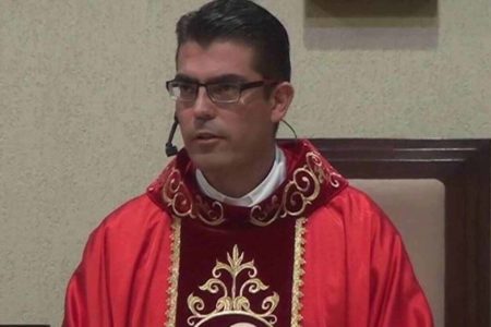 Imagem colorida mostra o padre Ferdinando Henrique Pavan Rubio, um homem branco de óculos de grau, vestido com roupas vermelhas dentro de uma igreja - Metrópoles