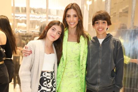 Foto de uma mulher com roupa verde abraçada de duas crianças, uma menina e um menino - Metrópoles