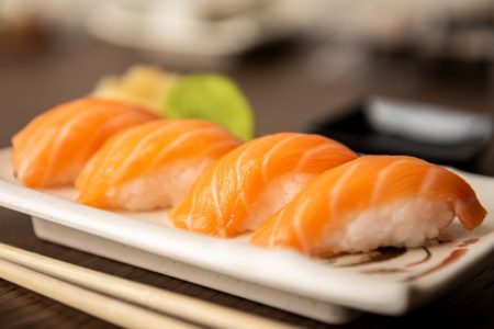 Fotografia colorida mostra quatro sushis de salmão enfileirados sobre um prato branco