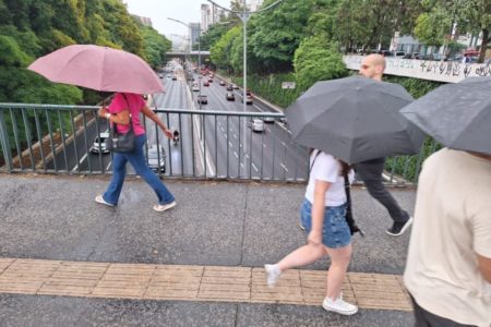 Imagem mostra pessoas caminhando com guarda-chuva - Metrópoles