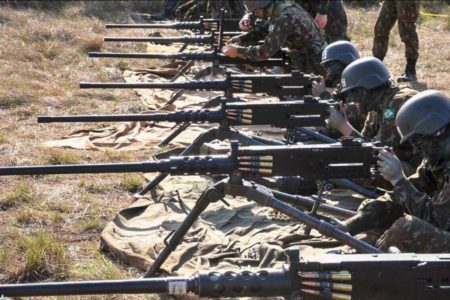 Militares com roupa camuflada lado a lado segurando metralhadoras antiaérea - Metrópoles