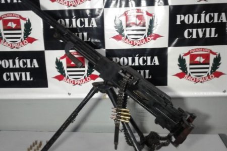 Metralhadora antiaérea sobre mesa em delegacia em frente a banner da Polícia Civil - Metrópoles