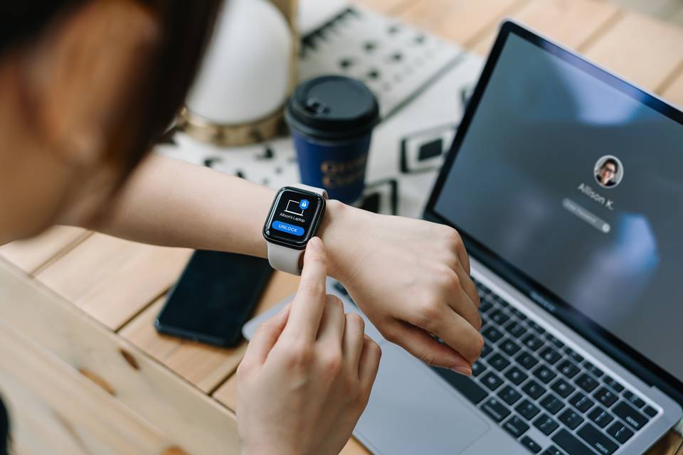 Foto colorida de mulher desbloqueando um smartwatch com uma escrivaninha ao fundo - Metrópoles